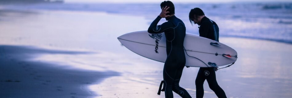 person walking on seashore holding surfboard